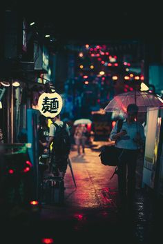 a woman holding an umbrella walking down a street at night