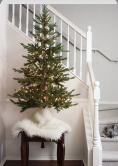 a small christmas tree sitting on top of a wooden stool next to a banister