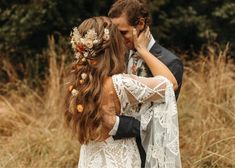 a bride and groom are standing in the tall grass with their arms around each other