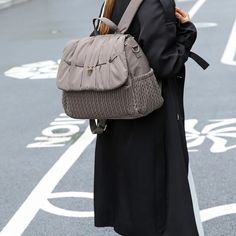 a woman is walking down the street with her handbag on her shoulder and looking at her cell phone