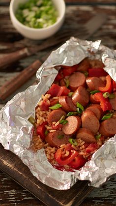 a hot dog covered in lots of toppings on top of tin foil next to some chopsticks