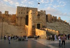 many people are walking around in front of a castle like structure with stairs and gates