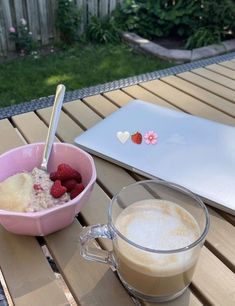 a cup of coffee and bowl of raspberries on a table with a laptop