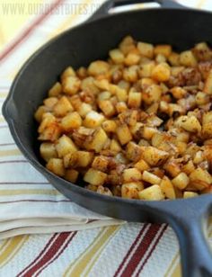 a skillet filled with cooked potatoes on top of a striped table cloth next to a wooden spoon