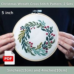 a person holding up a cross stitch christmas wreath