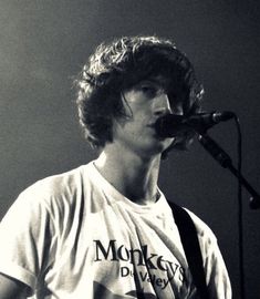 a man with a guitar and microphone in front of a microphone on the side of a stage