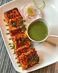 a white plate topped with food next to a bowl of green sauce