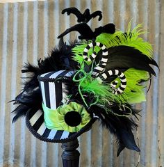 a black and white hat with green feathers on a stand in front of a corrugated wall