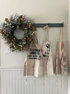 three aprons hanging on the wall next to a wreath and door hanger with flowers