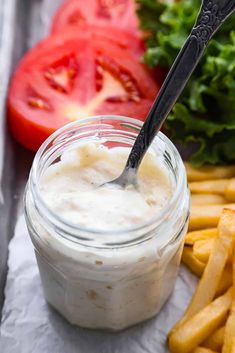 a jar filled with mayonnaise next to french fries and tomatoes on the side