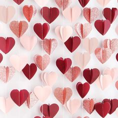 several hearts hanging from strings on a white wall with pink and red glittered paper