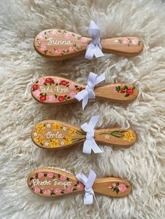 four wooden spoons with flowers and names on them sitting on a fluffy white surface