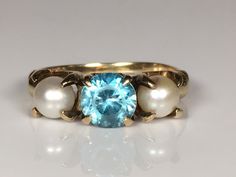 "Very pretty antique blue topaz and pearl ring from the Edwardian era in 10K yellow gold. This pretty ring features a natural blue topaz between two round natural pearls. The gemstones are prong set in a decorative mount with Deco detailing. The topaz measures 6mm; and the pearls measure 4.7mm. In excellent vintage condition. Ring size 5 1/4 and easily sized up or down several sizes. Please allow one week for sizing. One month layaway payment plans on items $500 and over available. Approximate A Blue Topaz And Pearl Ring, Sapphire Solitaire Ring, Blue Engagement Ring, Pretty Ring, Deco Blue, Sapphire Solitaire, Antique Blue, Edwardian Era, Pretty Rings