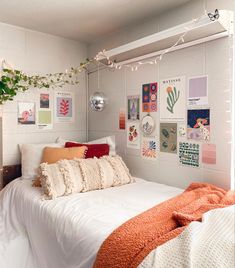 a white bed topped with lots of pillows next to a wall covered in pictures and plants