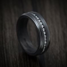 a black wedding band with white diamonds set in it on top of a wooden table