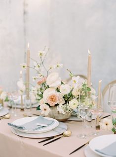 the table is set with white and pink flowers in vases, silverware, and candles