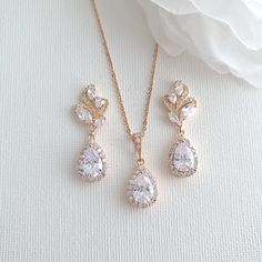 two pieces of jewelry sitting on top of a white cloth covered table next to a flower