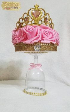 a pink rose covered cake under a glass dome on a white tablecloth with gold trim