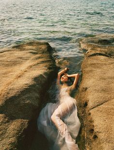 a woman laying on top of a rock next to the ocean