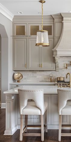 two white chairs sitting in front of a kitchen island with gold accents on the top