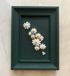 some daisies are in a green frame on the wall