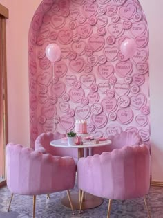 two pink chairs sitting next to each other in front of a wall with hearts on it