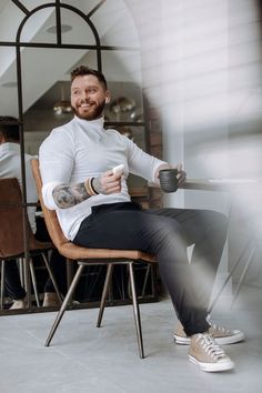 a man sitting in a chair holding a coffee cup and looking at the camera while smiling