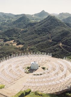 an aerial view of a circular structure in the middle of a field with mountains in the background