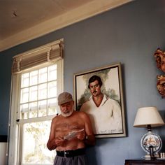 an older man standing in front of a painting on the wall next to a window