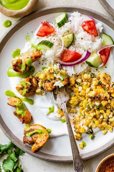 a white plate topped with rice and veggies next to a bowl of sauce