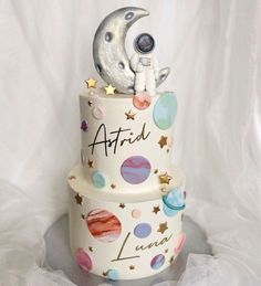 a three tiered cake decorated with planets and an astronaut on the top, sitting on a white table cloth