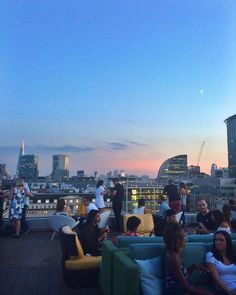 a group of people sitting on top of a roof next to tall buildings at sunset