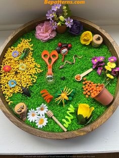 a wooden bowl filled with lots of fake flowers and gardening tools on top of green grass