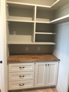 an empty walk in closet with white cabinets and wood counter tops on the bottom shelf