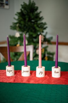 four candles sitting on top of each other in front of a table with a christmas tree