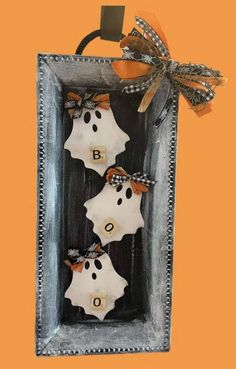 three halloween decorations in a frame on an orange background with the word boo spelled out