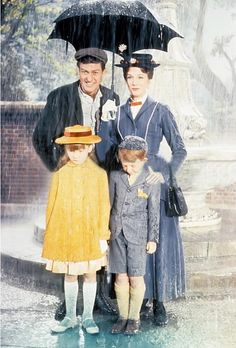 three people standing under an umbrella in the rain with two boys and one girl wearing hats