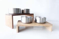 three metal bowls sitting on top of a wooden table next to two smaller silver pans