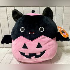 a black and pink stuffed animal with an orange pumpkin on it's back, sitting in front of a white wall