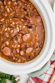 a white bowl filled with beans and sausage soup on top of a red checkered table cloth