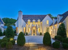 a large white house with lots of trees and bushes in front of it at night