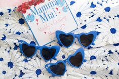 four blue heart shaped sunglasses sitting on top of a white lace tablecloth next to a sign that says mama mia made getting married