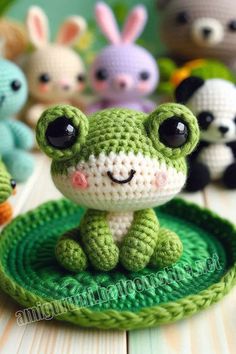 small crocheted frog sitting on top of a green plate with other stuffed animals in the background