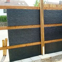 a dog is standing on the sidewalk next to a wooden fence with black stone panels