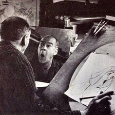 two men in an art studio looking at something on the easel while another man draws