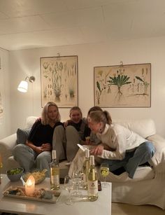 three women sitting on a couch in a living room with wine bottles and candles around them