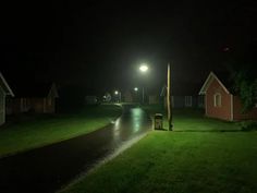 an empty street at night with no cars on the road and some houses in the background