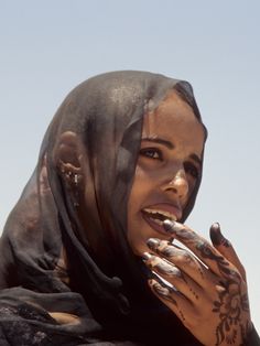 a woman with tattoos on her face and hands is standing in front of the sky