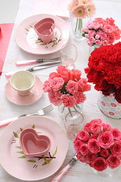 the table is set for valentine's day with pink and red flowers in vases