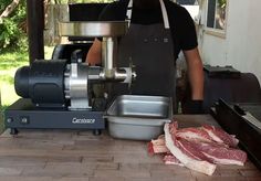 a man standing in front of a meat grinder with raw meat on the counter